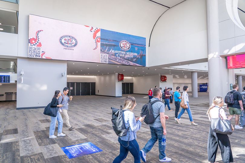 A large digital signage displays ads for local businesses while convention attendees move to their next meeting.